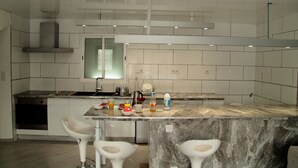 A modern kitchen with white cabinetry, a marble countertop, and a built-in oven. There are bar stools and a window above the sink. - Your little paradise;) (ESPONDEILHAN)