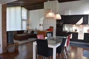 Una cocina moderna con armarios oscuros, un comedor con mesa de vidrio y una sala de estar con sofá y chimenea.