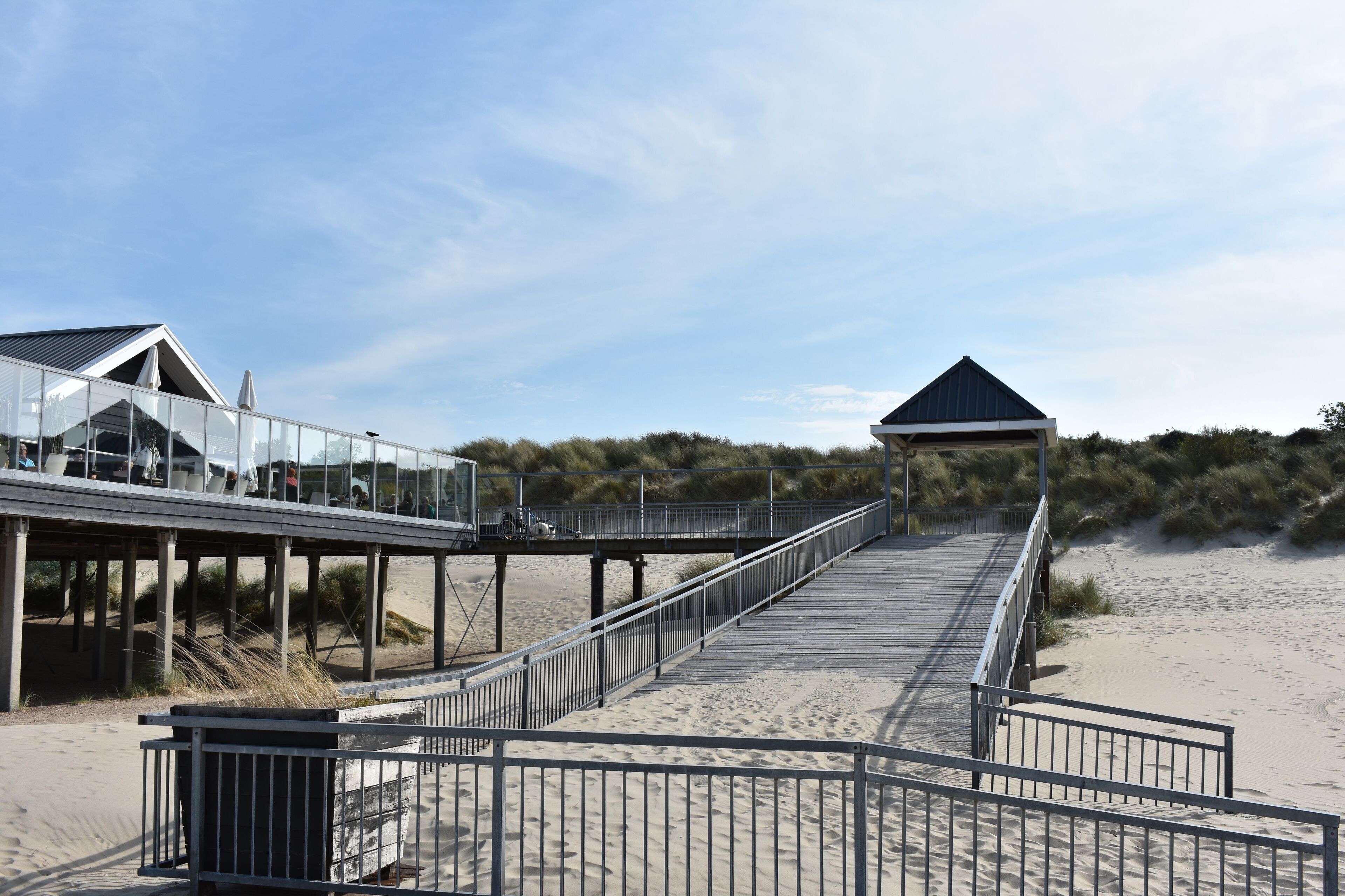 A beach boardwalk with a glass-walled building and a covered pavilion.