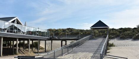 A beach boardwalk with a glass-walled building and a covered pavilion.