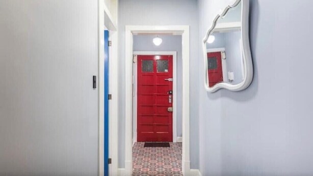 Um corredor com uma porta vermelha, uma porta azul e um espelho na parede.