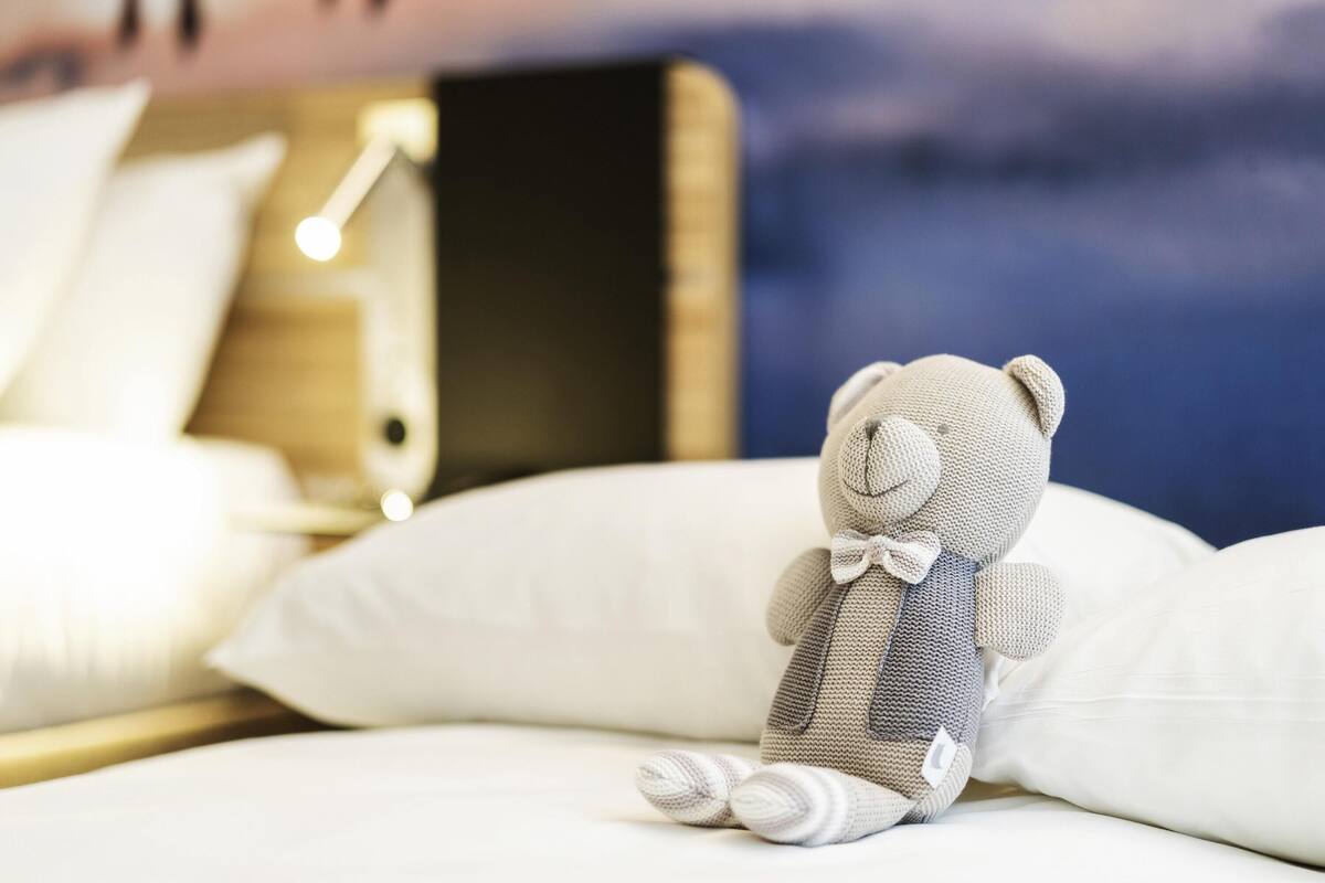 A plush toy on a bed with white pillows and a headboard.