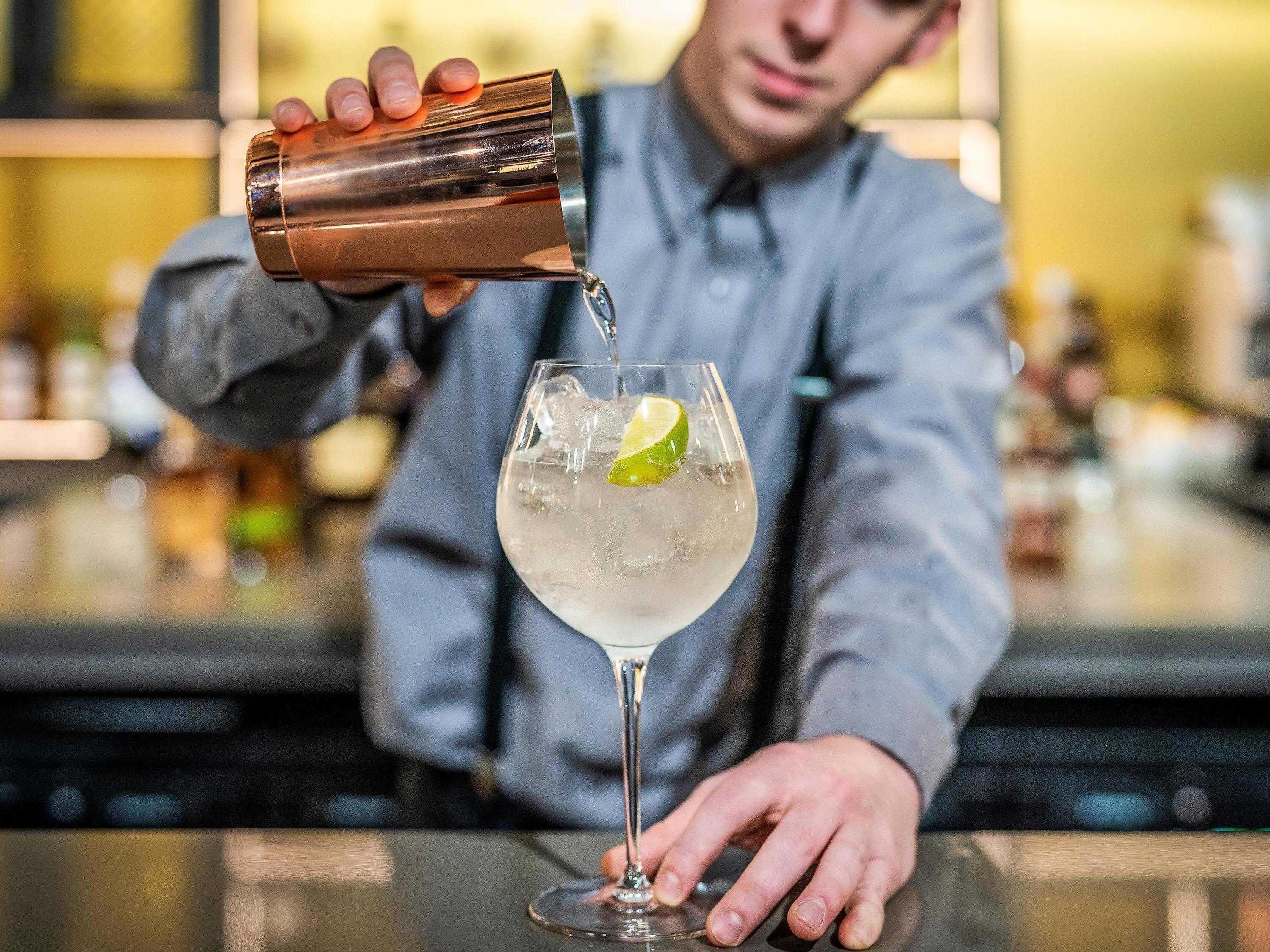 A bartender pouring a drink into a glass with a lime wedge.