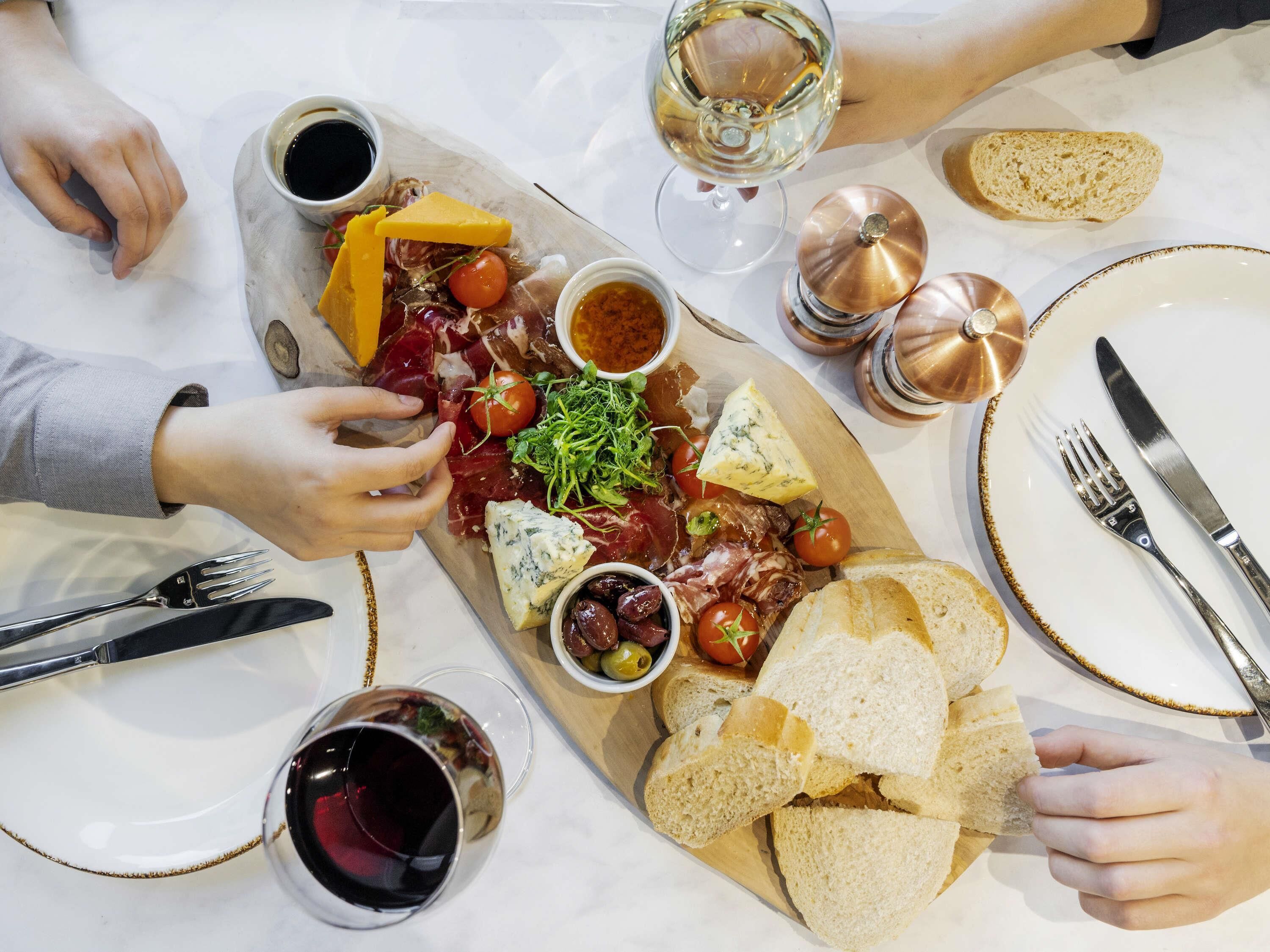 Pöydällä on monenlaista syötävää, kuten juustoja, lihatuotteita ja leipää, sekä viinilaseja ja ruokailuvälineitä.