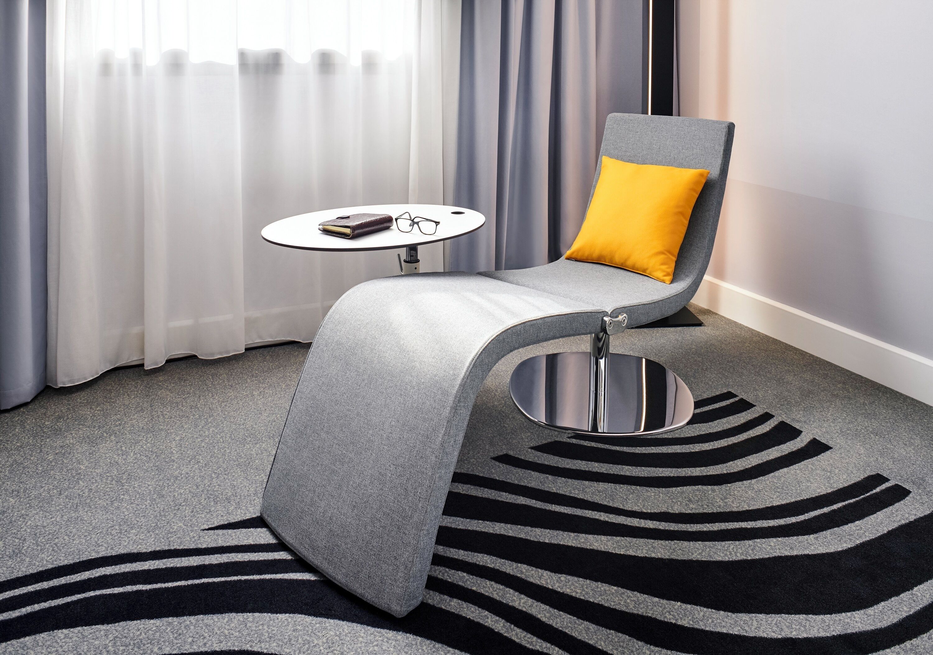 A modern room with a grey sofa, a yellow pillow, a round table with glasses and a book, and a zebra-patterned rug.