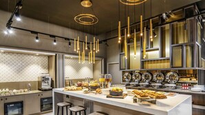 A modern kitchen with a central island, bar stools, and a variety of breakfast items. - Novotel Leicester (Leicester)