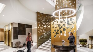 A modern lobby with a reception desk, a staircase, and a seating area. - Novotel Leicester (Leicester)
