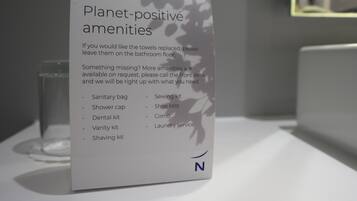 Señal que detalla servicios ecológicos en una habitación de hotel, incluyendo bolsa sanitaria, gorro de ducha, kit de aseo dental, set de tocador, kit de afeitar, kit de costura, funda para zapatos, peine y servicio de lavandería.