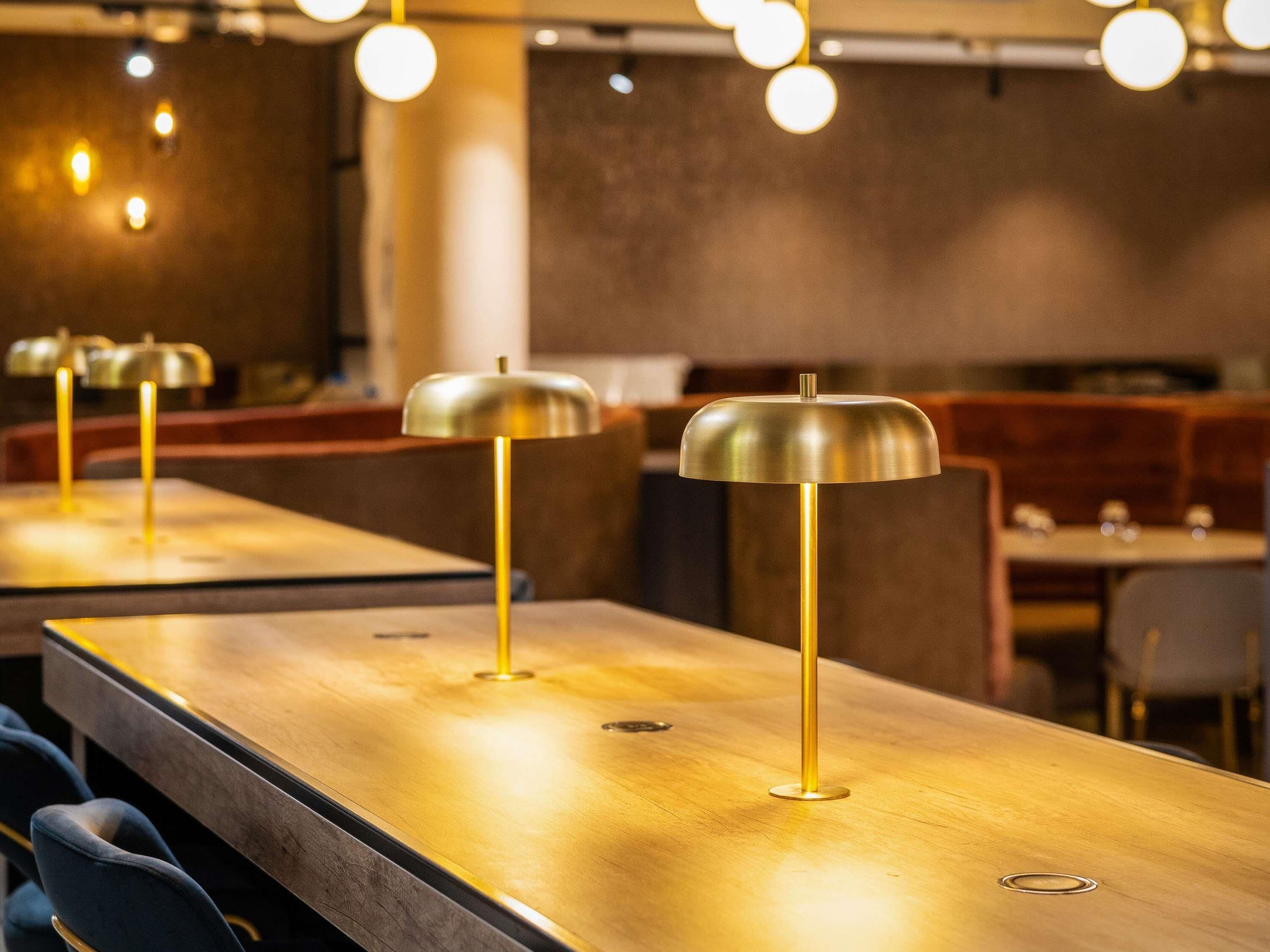 A restaurant interior with long tables, chairs, and pendant lighting.