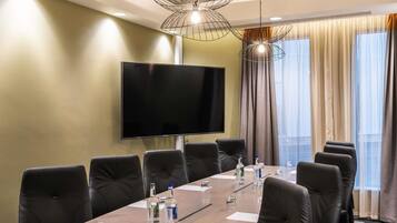 A conference room with a long table, black leather chairs, a flat-screen TV, and a modern pendant light.