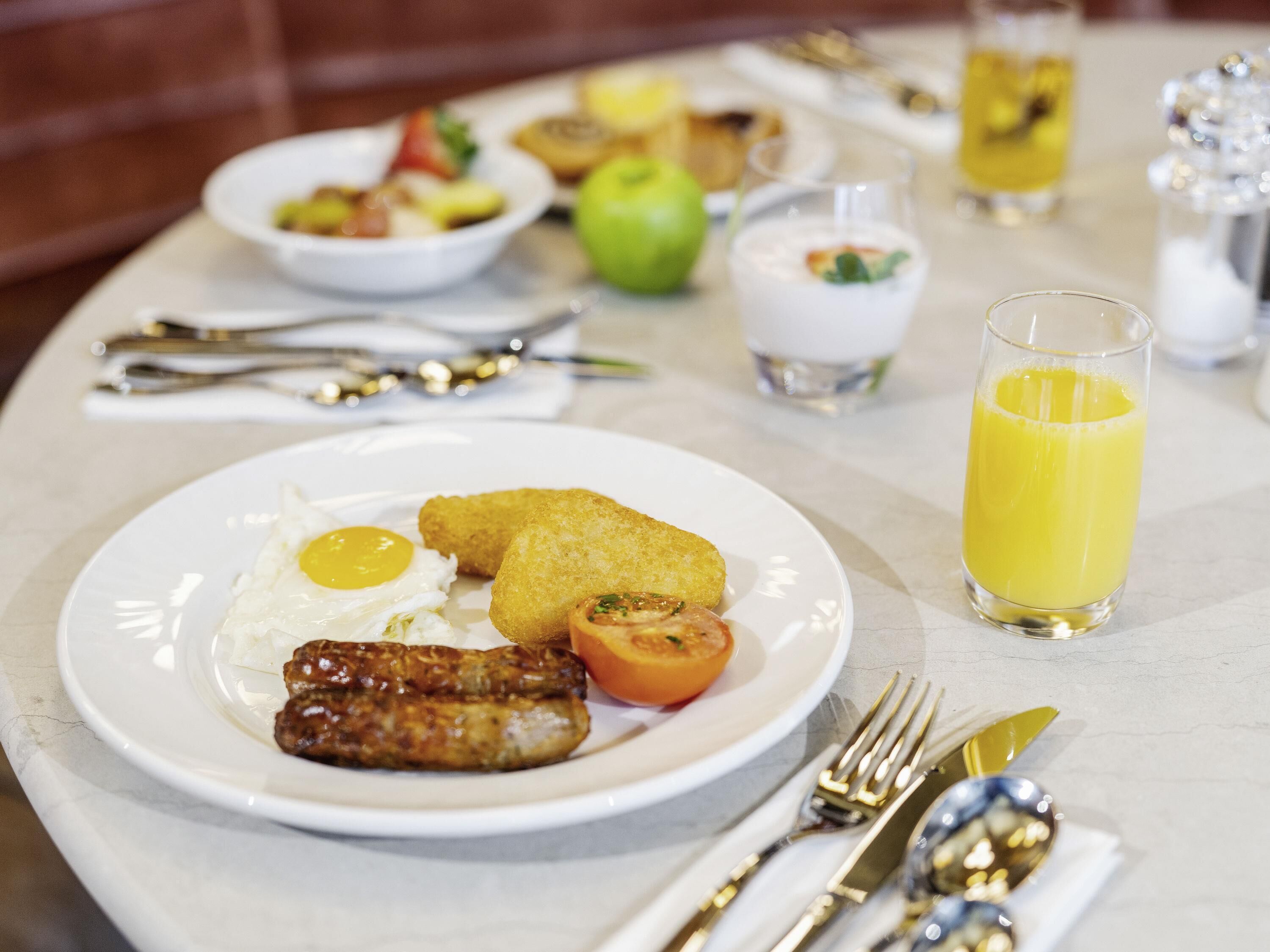 A breakfast setting with plates of food, a glass of orange juice, and dining utensils.