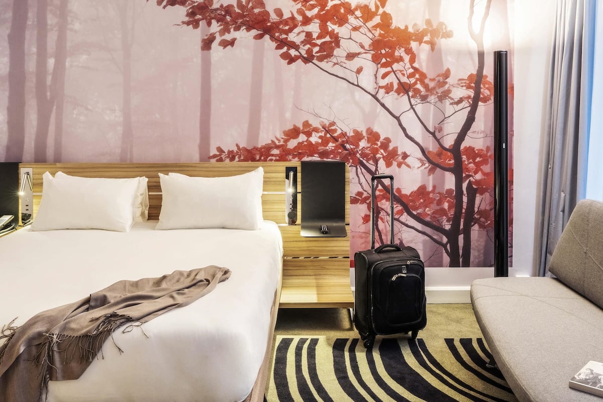 A hotel room with a bed, a TV, a suitcase, and a sofa.
