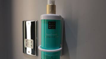A teal bottle of hand wash soap labeled "Rituals" on a wall.