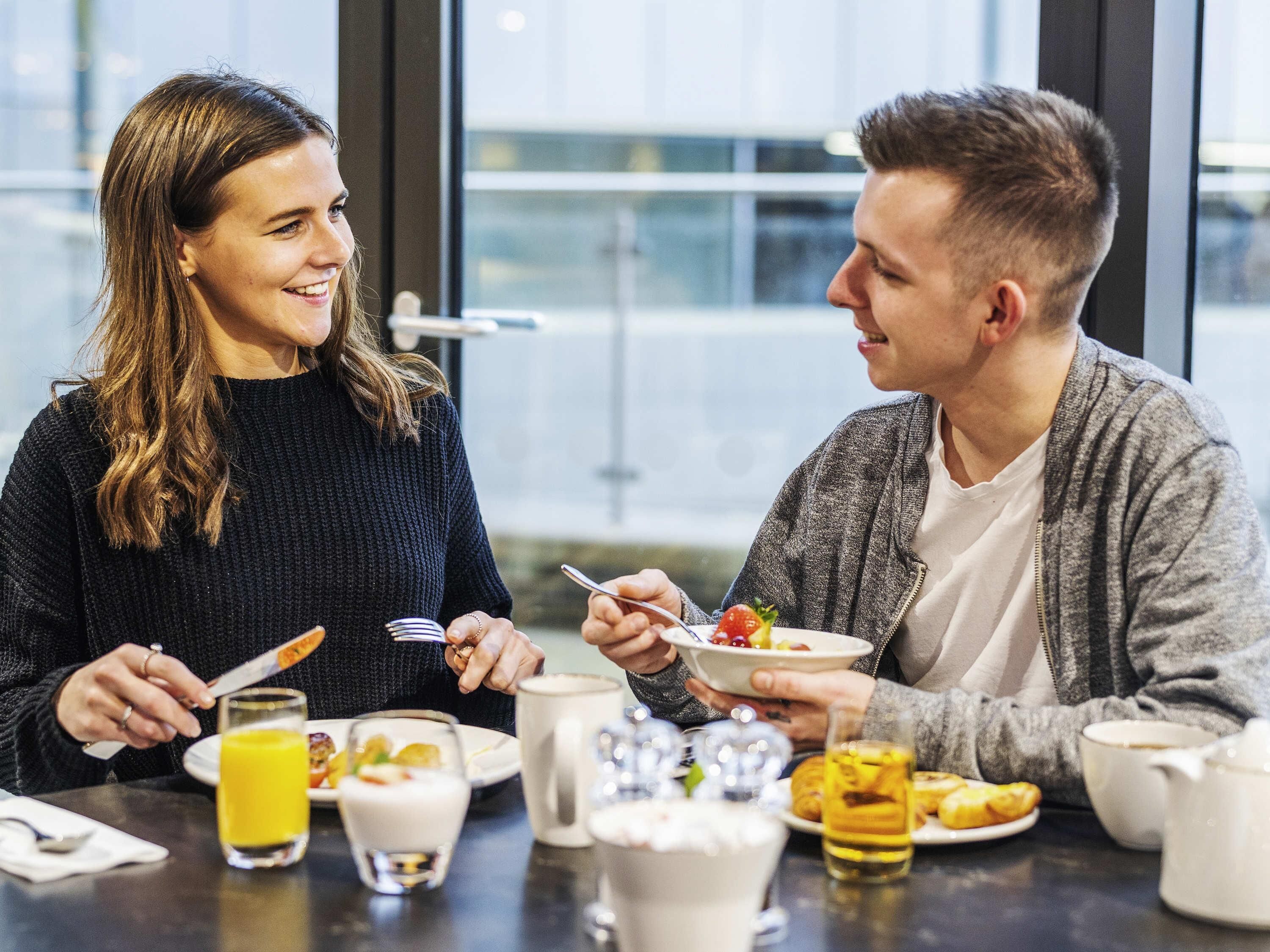 Two people dining at a table with various breakfast items, including pancakes, a glass of orange juice, and a cup of coffee.