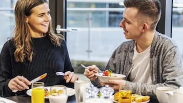 Twee personen dineren aan een tafel met diverse ontbijtartikelen, zoals pannenkoeken, een glas sinaasappelsap en een kop koffie.