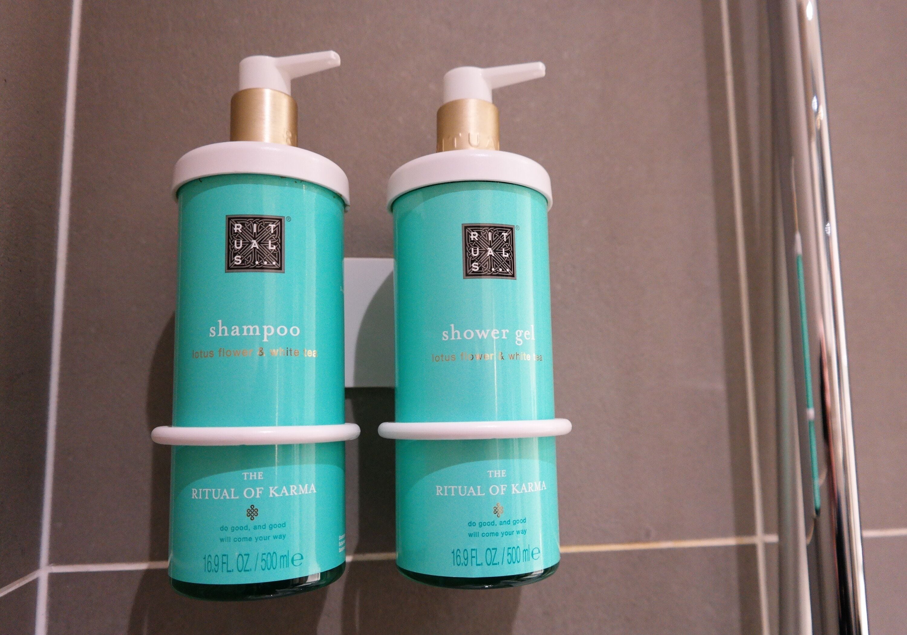 Two bottles of 'The Ritual of Karma' shampoo and shower gel on a tiled wall.