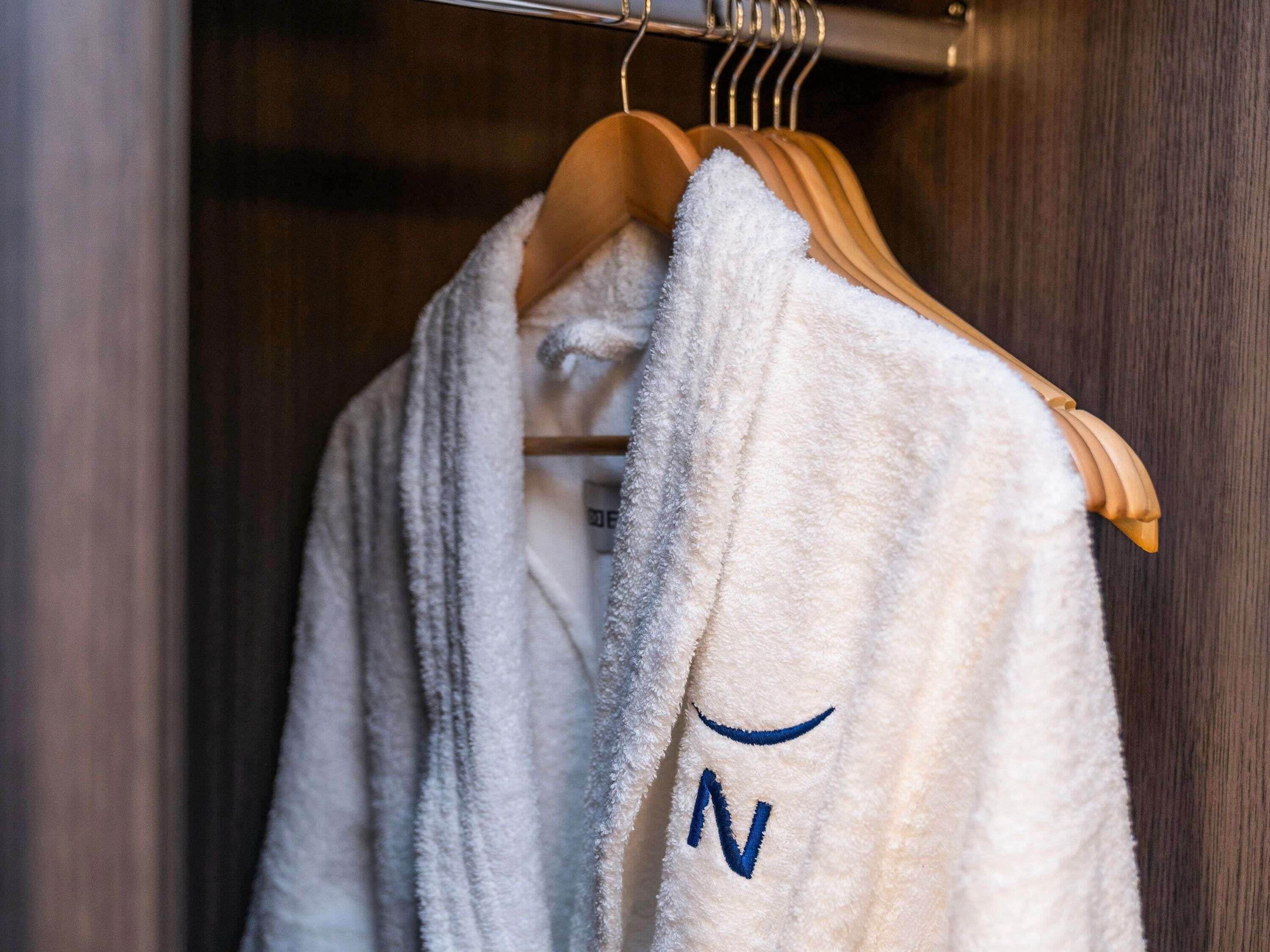 A white robe with a blue letter 'N' hanging on a wooden hanger.