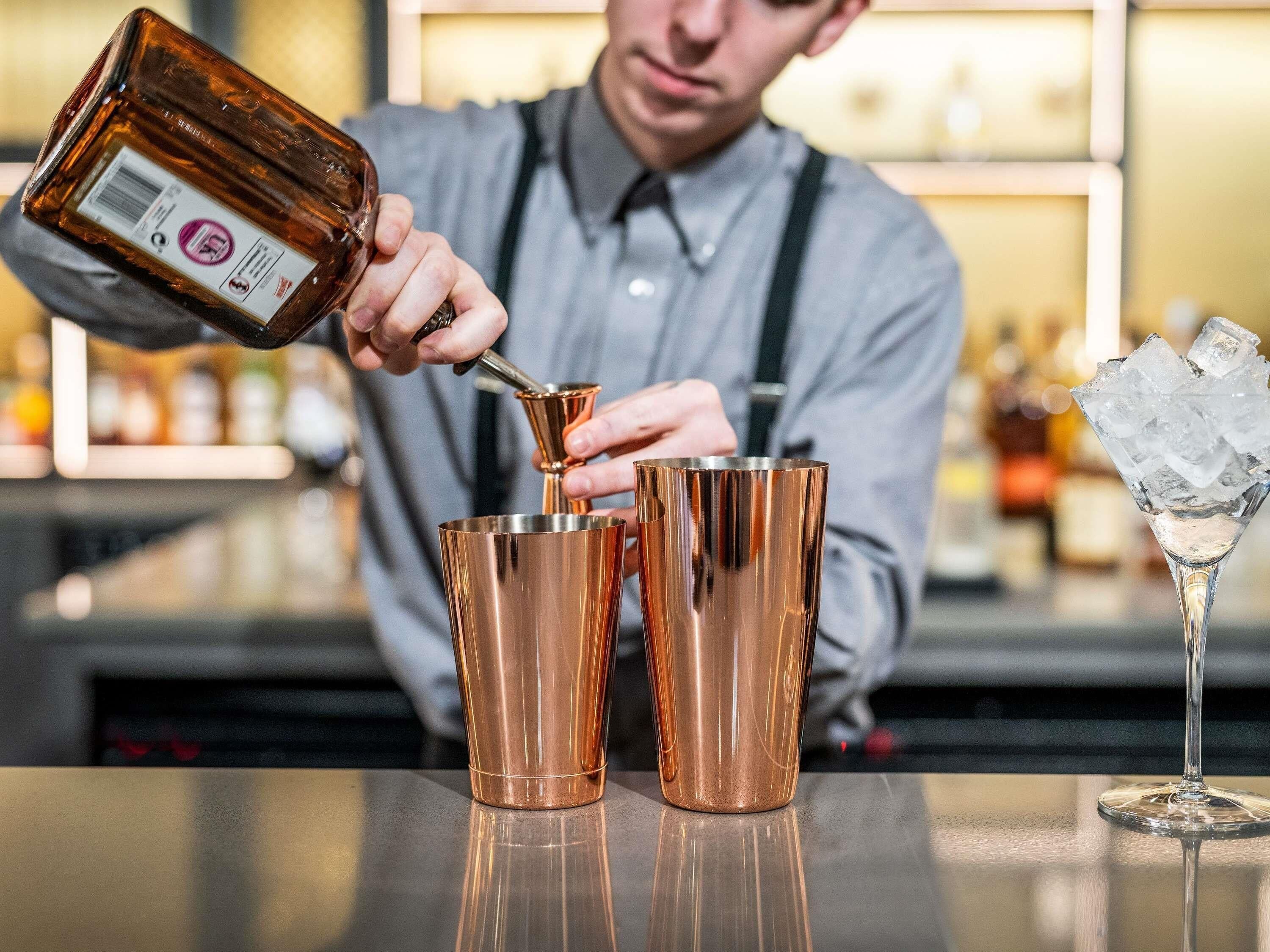 A bartender pouring a drink into a copper shaker.
