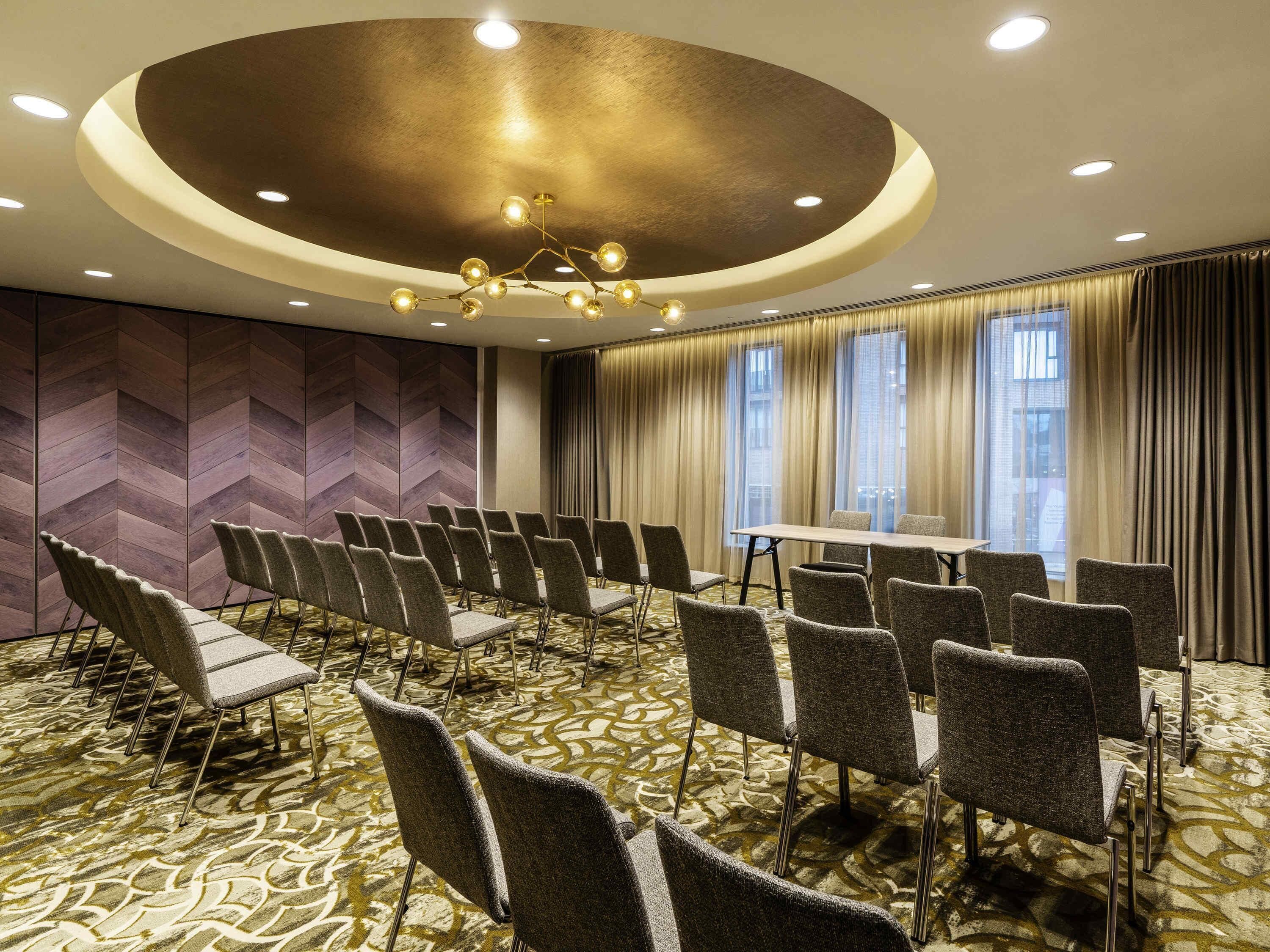 Un salón de conferencias con una lámpara moderna, una mesa grande y una alfombra estampada.