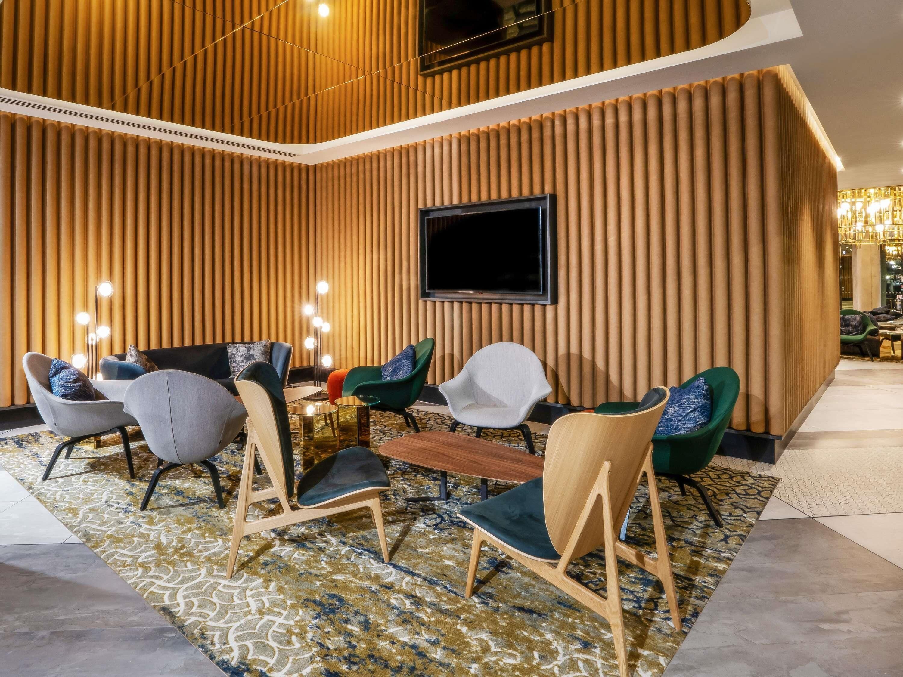 A modern lounge area with a variety of seating options, a flat-screen TV mounted on the wall, and a patterned carpet.