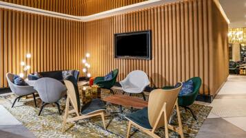 A modern lounge area with a variety of seating options, a flat-screen TV mounted on the wall, and a patterned carpet.