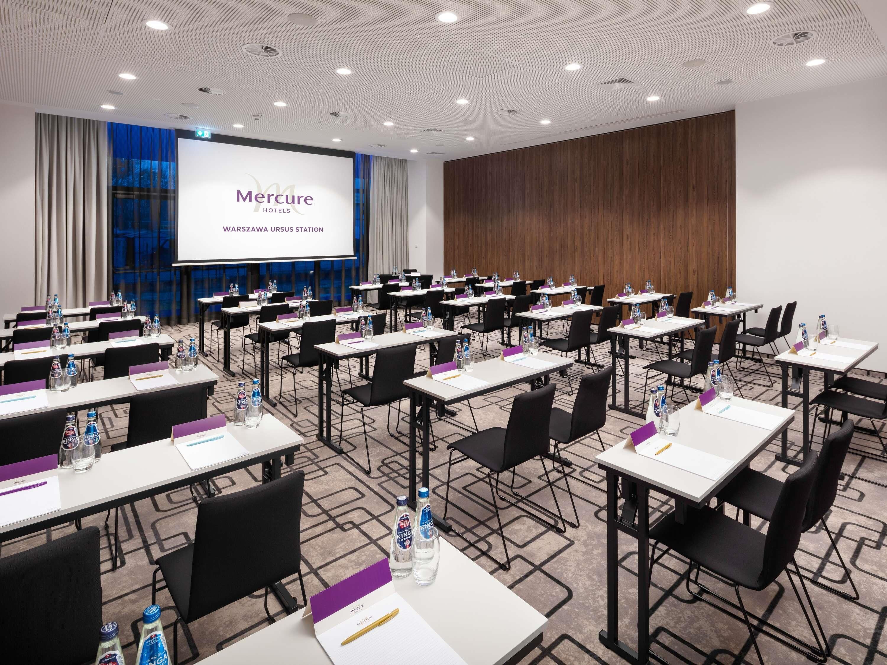 A conference room with tables, chairs, and a presentation screen at Mercure Warszawa Ursus Station.