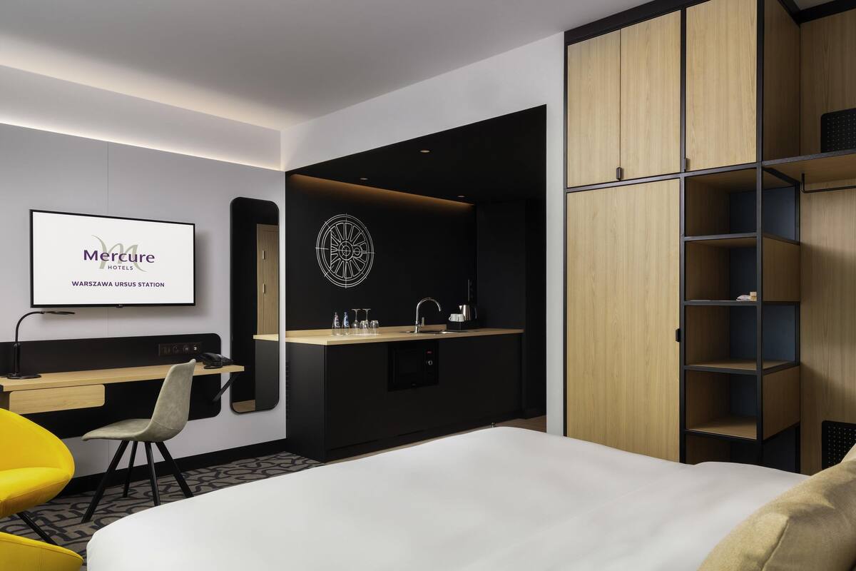 Une chambre d’hôtel comprenant un lit, un bureau, une chaise, une petite kitchenette et une armoire.