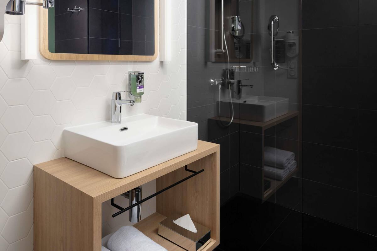Une salle de bain moderne avec un lavabo blanc, un meuble-lavabo en bois et une cabine de douche en verre.