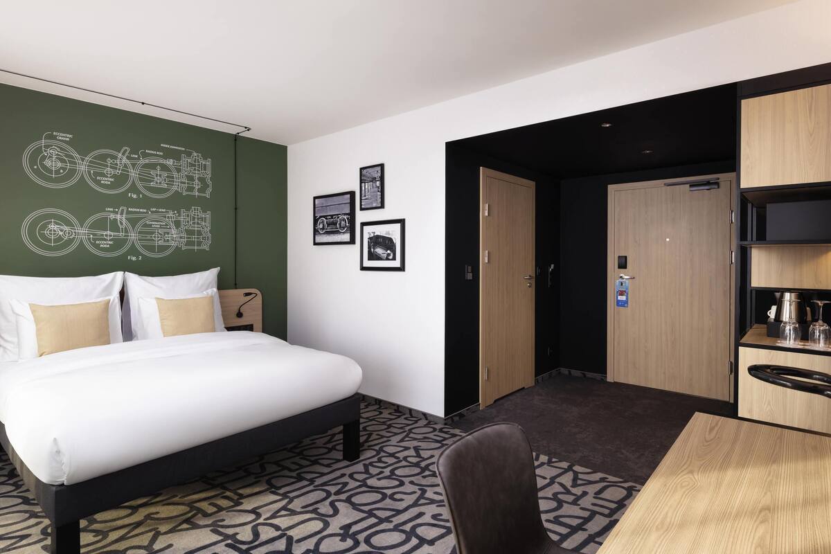 Une chambre d’hôtel équipée d’un lit, d’un bureau, d’une chaise, d’une armoire et d’un mur orné de plans techniques.