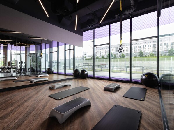 A modern gym with exercise equipment, large windows, and a view of the city. - Mercure Warszawa Ursus Station (Warsaw)