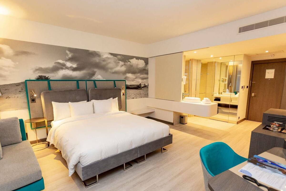 Ein modernes Hotelzimmer mit Bett, Schreibtisch, Stuhl und einem Badezimmer mit Spiegel sowie einer Wandmalerei.