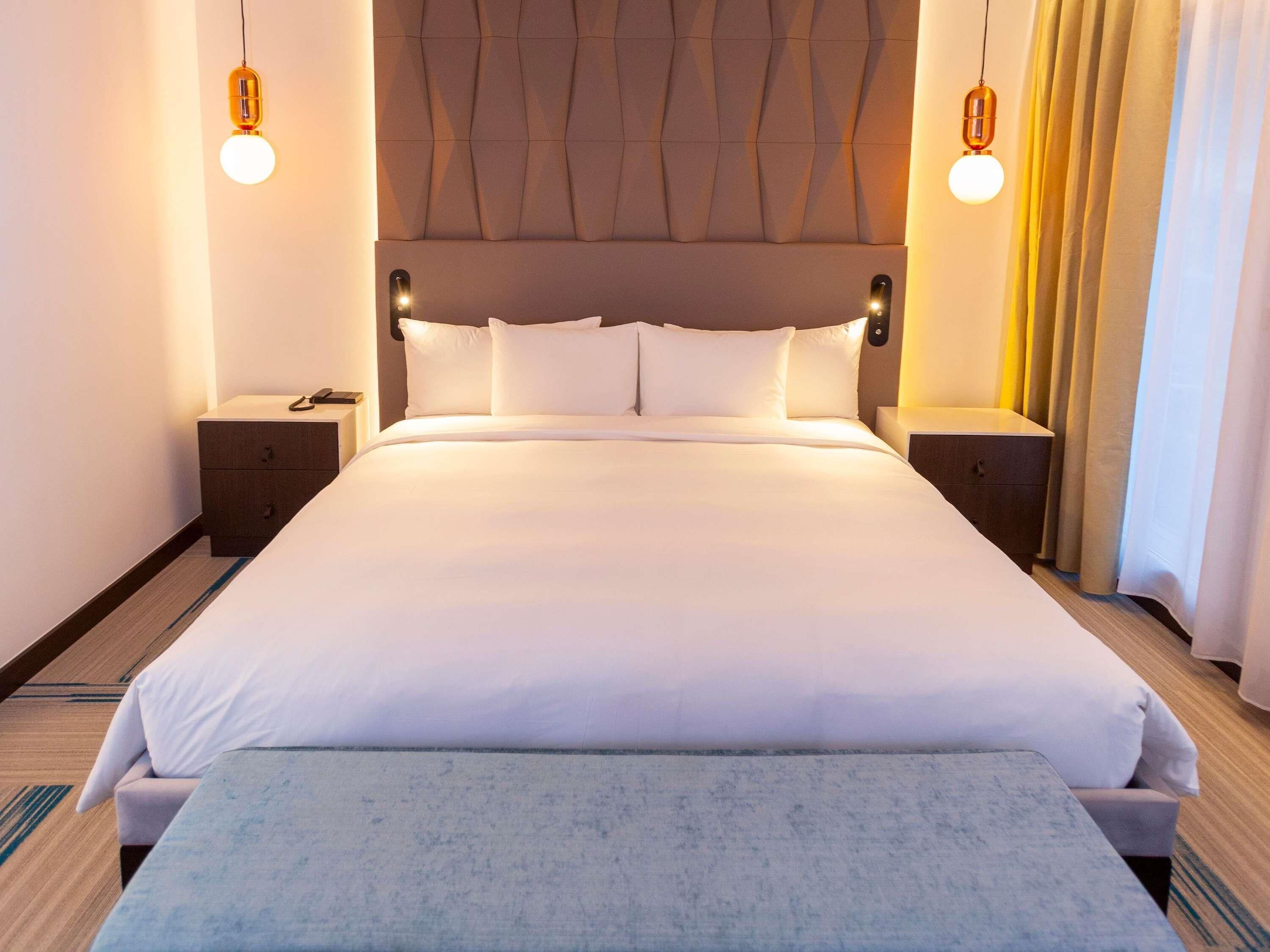 A large bed with a headboard, two bedside tables, and a bench at the foot of the bed.