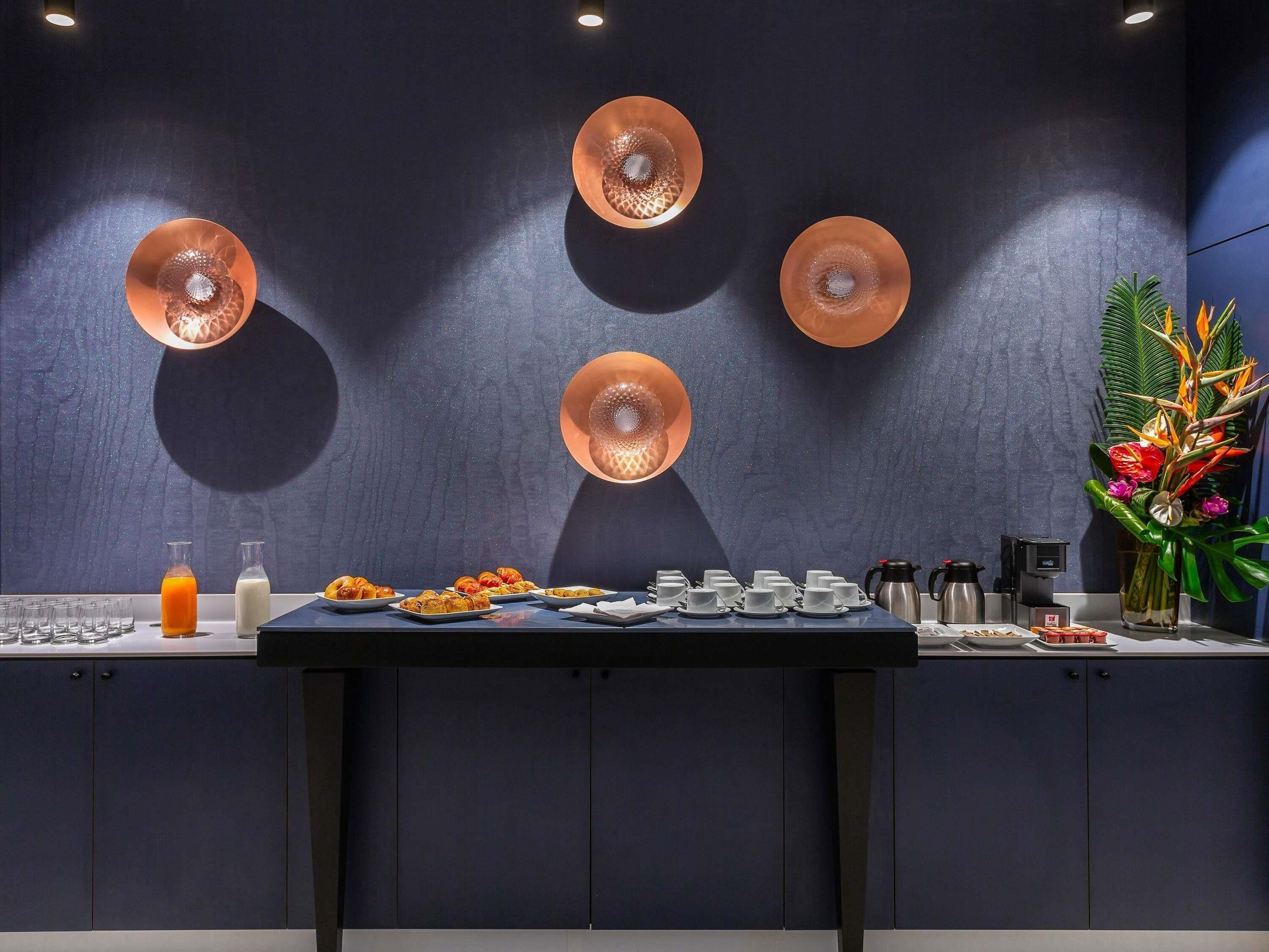 Un bufé de desayuno con diversos platos, una estación de café e iluminación decorativa en las paredes.