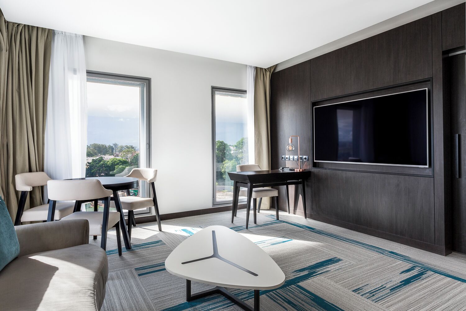 Una habitación de hotel moderna con una televisión grande, un sofá, una mesa de comedor y sillas.