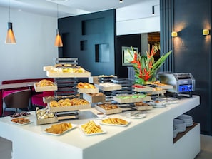 A buffet with various food items, a coffee machine, and a decorative plant. - Novotel Convention And Spa (Antananarivo)