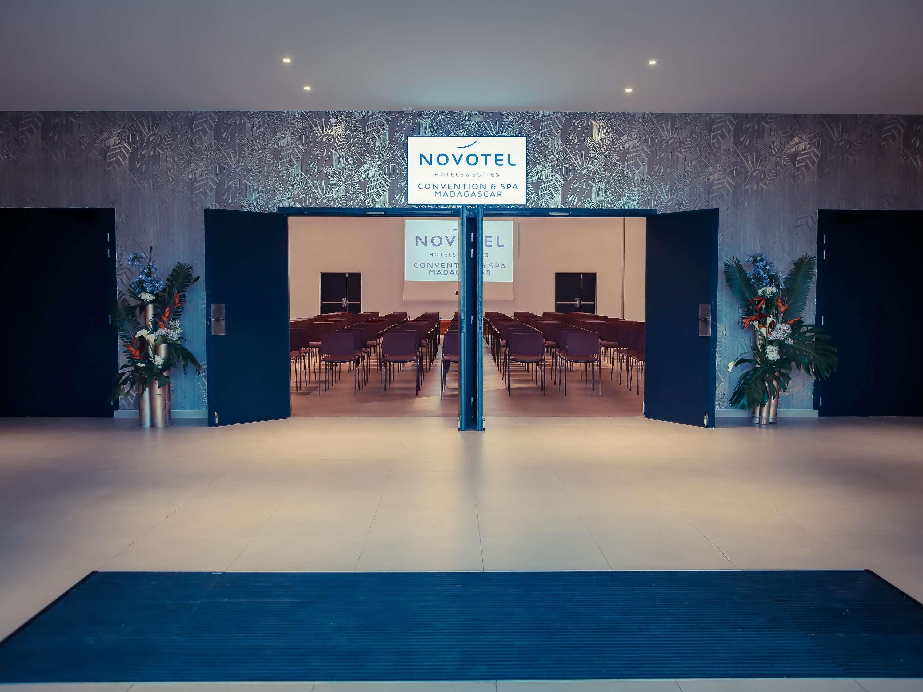 Entrada de un hotel con un cartel que dice 'NOVOTEL' y una sala de conferencias con sillas.