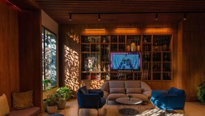 A modern living room with a large TV, wooden shelves, and comfortable seating. - Novotel Convention And Spa (Antananarivo)