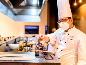 A chef in a white uniform with a chef's hat, holding a teapot. - Novotel Convention And Spa (Antananarivo)