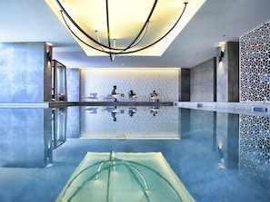 Une piscine intérieure moderne, avec une eau cristalline, un plafond au design géométrique et un mur texturé en arrière-plan.