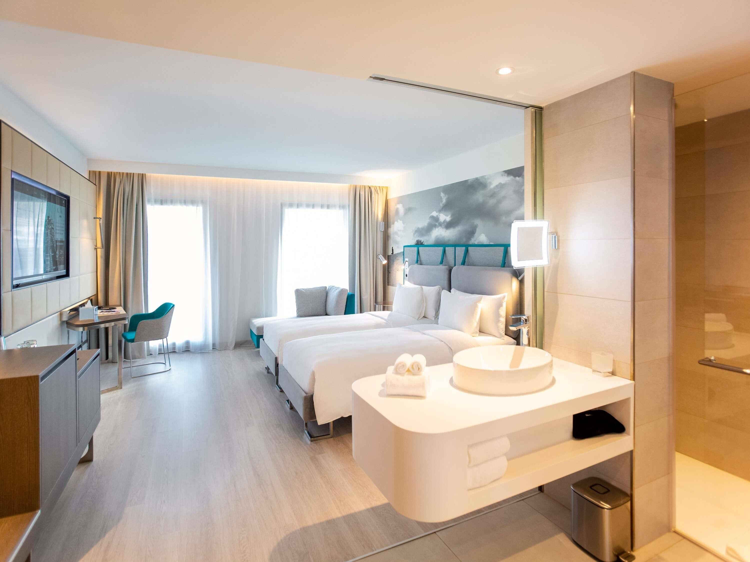 A hotel room with a bed, a desk, a chair, a bathroom, and a view of the city.