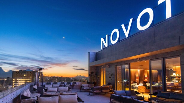 A rooftop terrace with outdoor seating, a large illuminated sign, and a cityscape view. - Novotel Convention And Spa (Antananarivo)