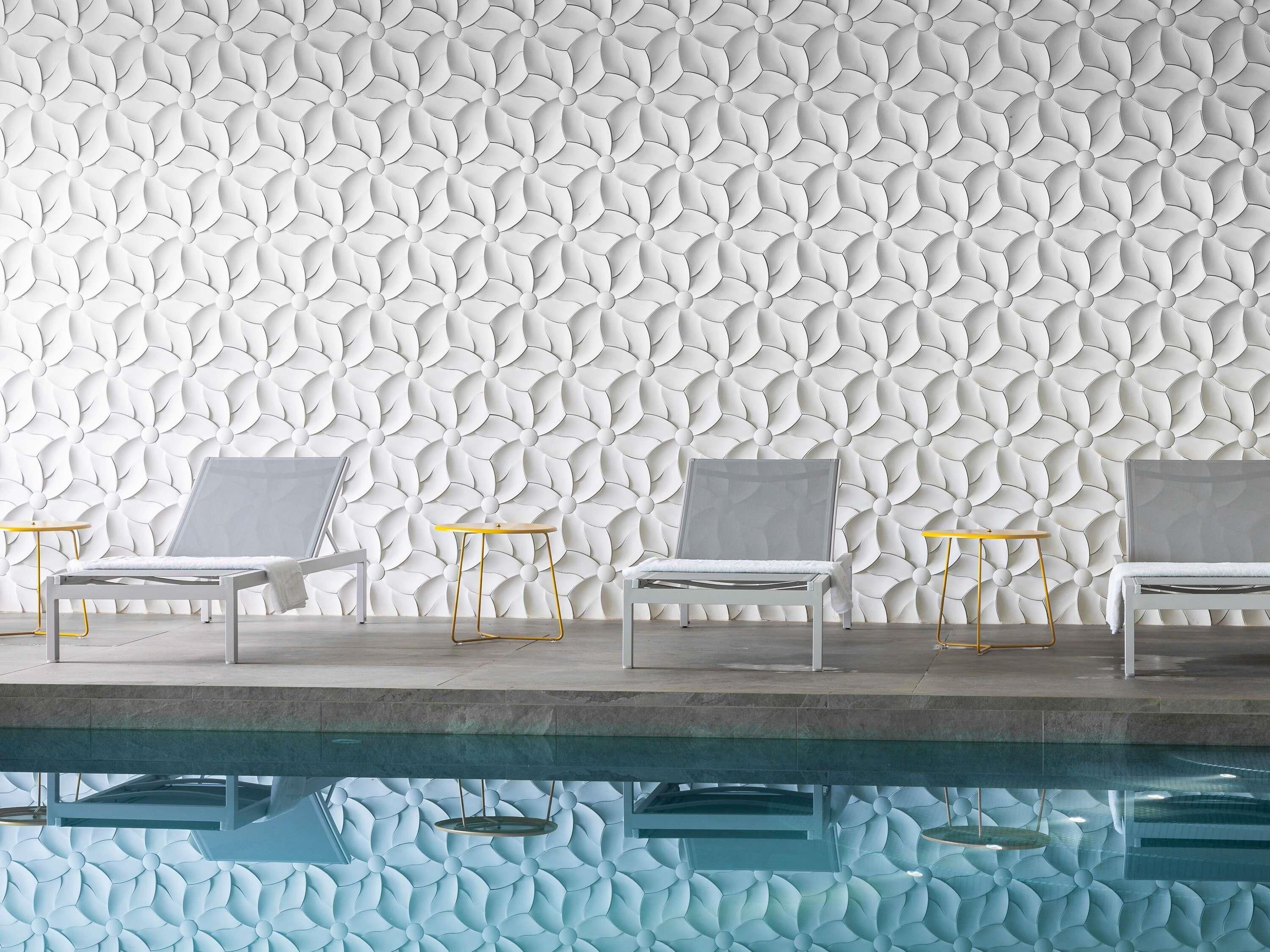 A poolside area with white lounge chairs and a patterned wall.