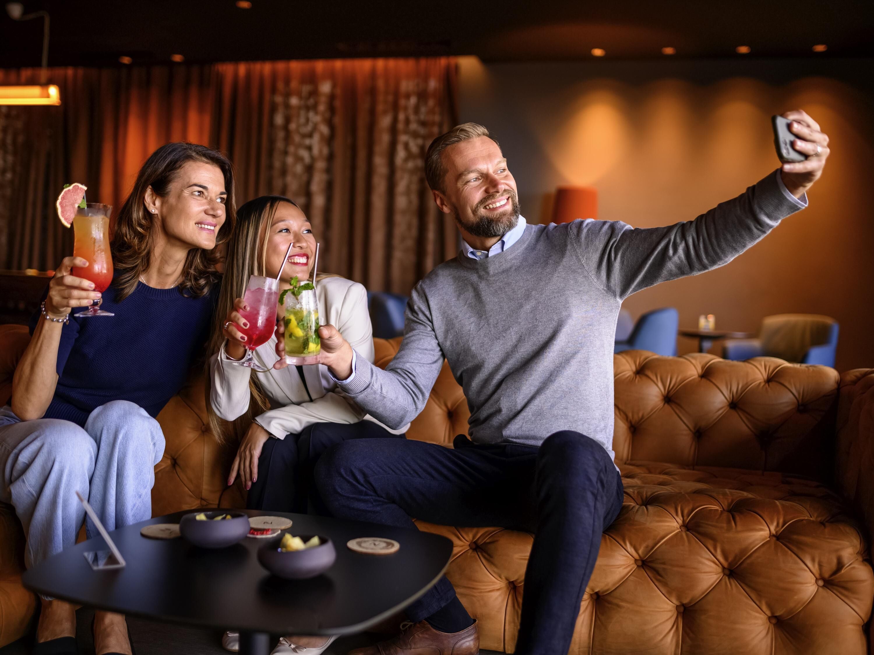 Three people sitting on a brown leather couch in a room with a small round table in front of them.