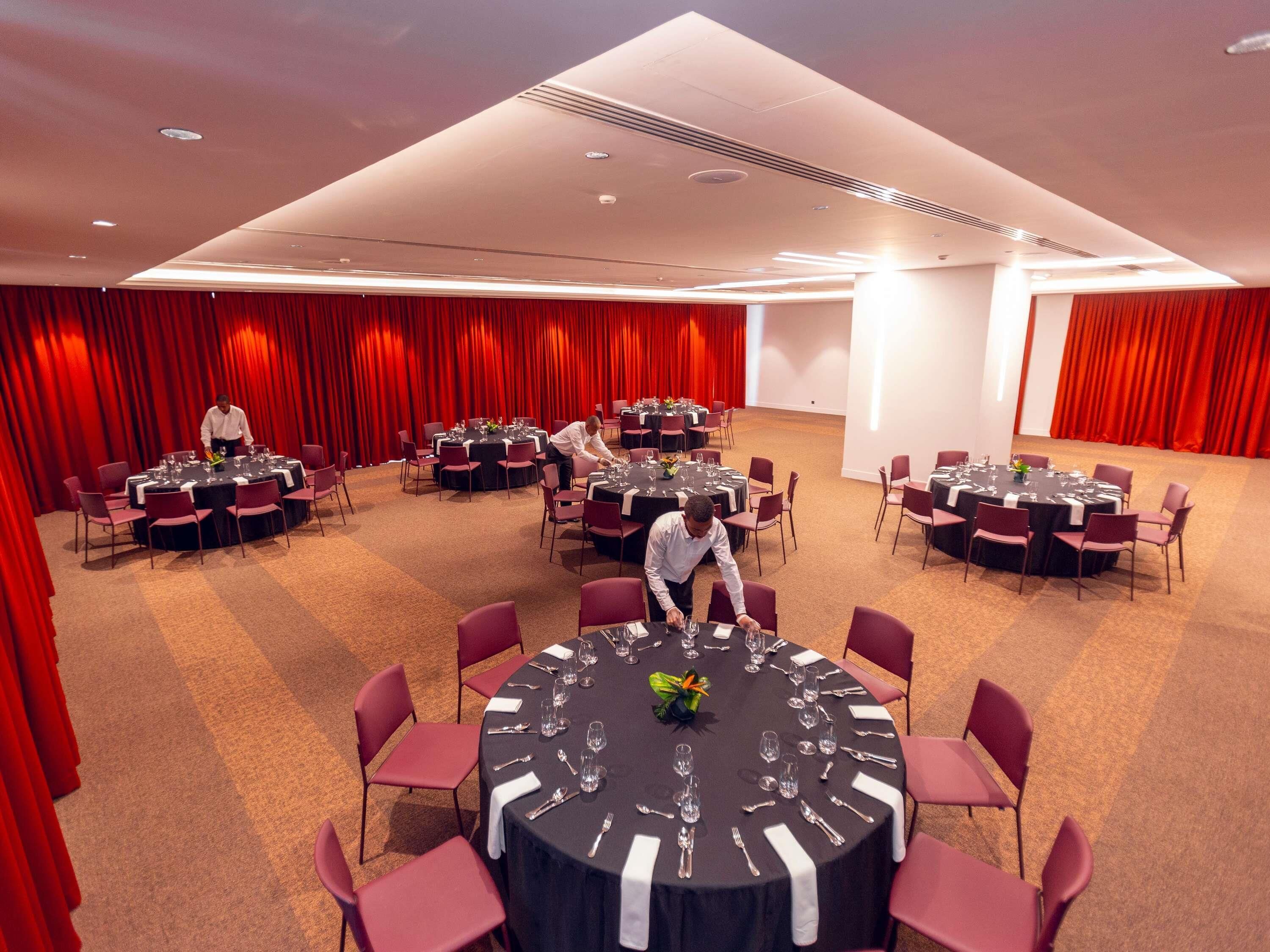 Une salle de conférence avec des tables rondes, des rideaux rouges et un sol recouvert de moquette.