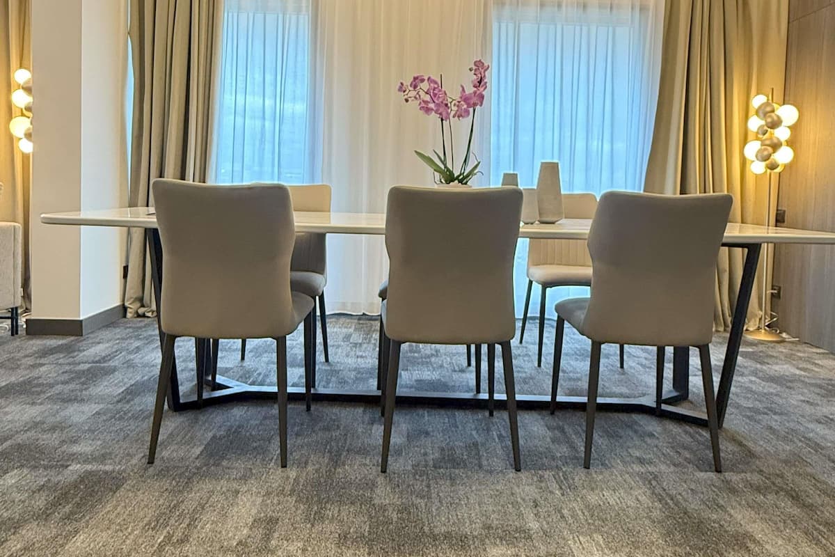 Une chambre d’hôtel avec une table à manger, trois chaises, un vase de fleurs et une lampe.