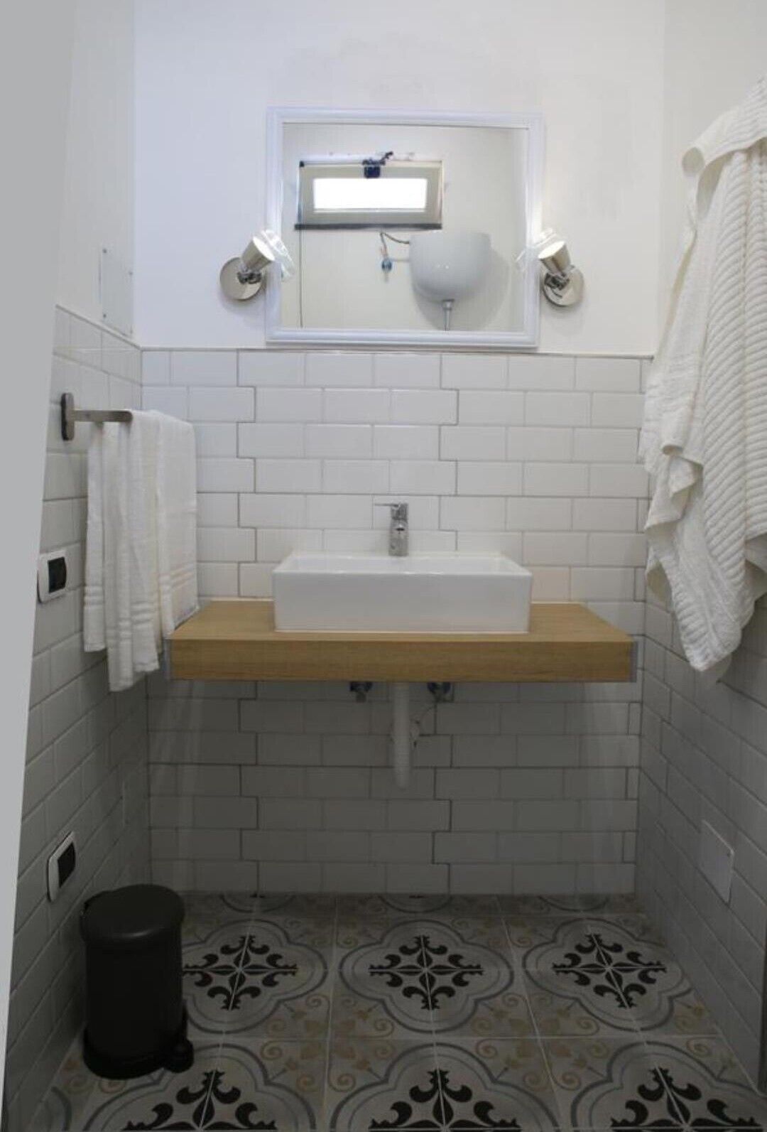 Une petite salle de bain avec un lavabo blanc, un miroir au-dessus et des carreaux décoratifs sur le sol.