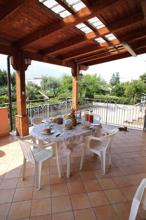 A covered outdoor dining area with a table set for two, surrounded by chairs, under a wooden roof with skylights. - Villa Rosa Pompei Studios (Scafati)