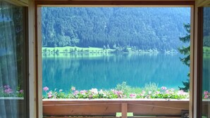 A view of a lake surrounded by forest, with a wooden deck in the foreground. - Chalets Zöhrer - Wohnen am Wasser (Weissensee)