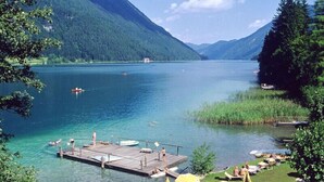 A lakeside view with a dock, boats, and people swimming. - Chalets Zöhrer - Wohnen am Wasser (Weissensee)