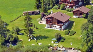 A large house with a balcony, surrounded by a well-maintained lawn and a dock with boats. - Chalets Zöhrer - Wohnen am Wasser (Weissensee)